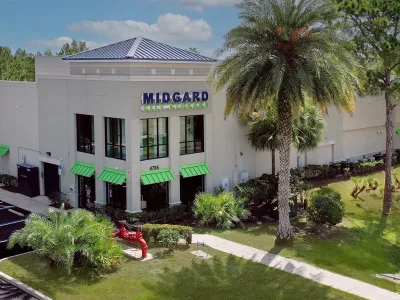 Midgard Self Storage building with green awnings, palm trees, and landscaped surroundings under a blue sky