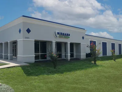Midgard Self Storage building with white walls, blue accents, and a green lawn under a partly cloudy sky.