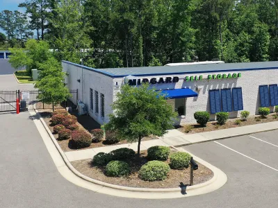 Midgard Self Storage building with parking lot, greenery, and secure gated entrance on a sunny day.
