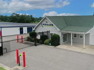 Midgard Self Storage facility with gated entrance, office building, and multiple storage units under a partly cloudy sky.