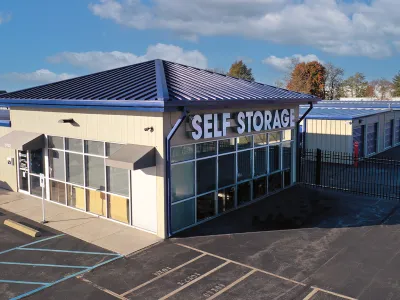 Modern self storage facility with large windows, blue metal roof, and outdoor storage units under clear sky.