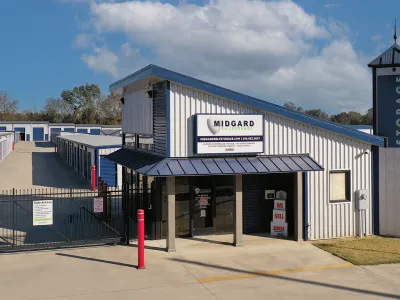 Modern self-storage facility with gated access, office building, and multiple storage units under a partly cloudy sky.