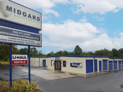 Midgard Self Storage facility with office, blue storage units, U-Haul rental sign, and contact information under a partly cloudy sky