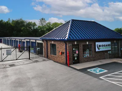 Storage facility with gated entrance, brick office building, and blue roof under a partly cloudy sky