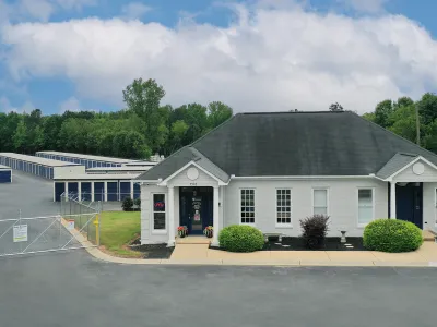 Storage facility office building with gated access and rows of storage units under blue sky with clouds.