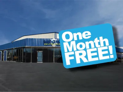 Self storage facility with blue exterior and promotional sign offering one month free rental under a clear sky.