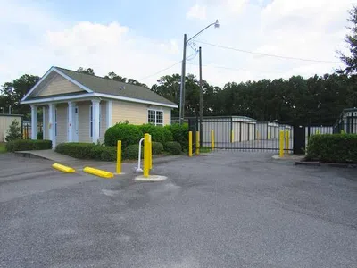 Secure self-storage facility with gated entrance, yellow bollards, and a small guardhouse on a clear day.