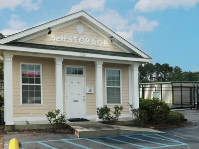 Secure self-storage facility with gated entrance, yellow bollards, and a small guardhouse on a clear day.