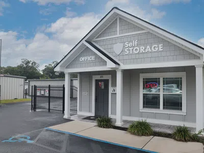 Modern gray self storage office building with white trim and an open sign on the window under a blue sky.