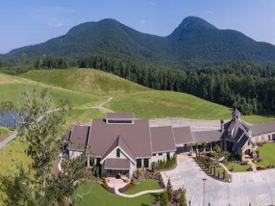 Aerial view of a countryside building complex with mountains and greenery under a clear blue sky.