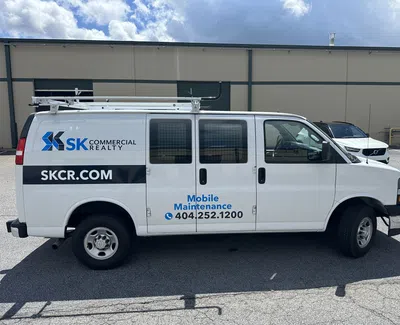 White SK Commercial Realty maintenance van parked outside with company logo and contact info on side.
