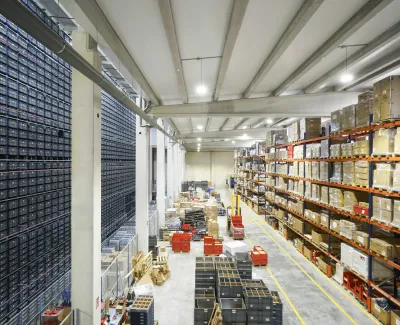 Large organized warehouse with tall shelves stocked with boxes and bins, featuring automated storage systems.