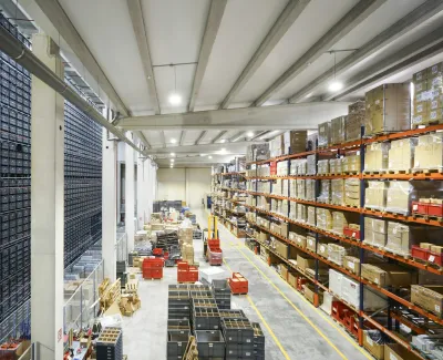 Large organized warehouse with tall shelves stocked with boxes and bins, featuring automated storage systems.