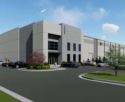 Modern industrial warehouse building with parking lot, cars, and landscaping under a blue sky.