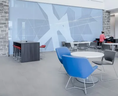 Modern spacious lounge area with blue chairs, tables, red stools, and geometric wall art in a bright atrium.