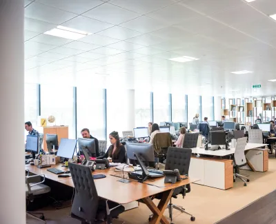 Bright open-plan office with employees working at desks equipped with computers and office chairs.