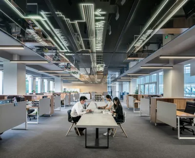 Modern office with an open layout, illuminated ceiling designs, and professionals working at a central table.