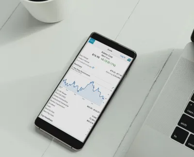 Smartphone displaying Roblox Corp stock chart and information next to a laptop and coffee cup on white table