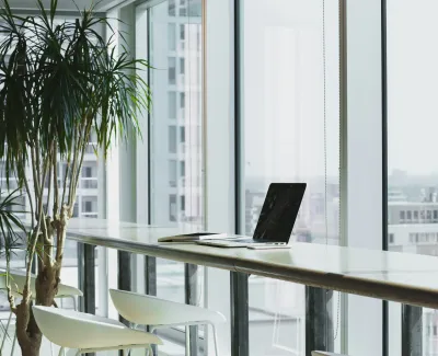 a table with a laptop and chairs by a window