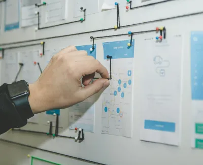 Person pinning a route on a map connected with strings on a planning board with documents and details.