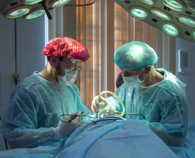 Two surgeons in protective gear performing surgery under bright operating room lights.