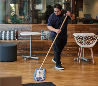 Man mopping a clean wooden floor in a modern cafe with tables and chairs in the background