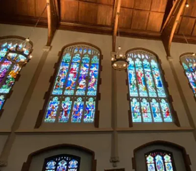 Interior view of a church with large colorful stained glass windows and wooden ceiling beams.