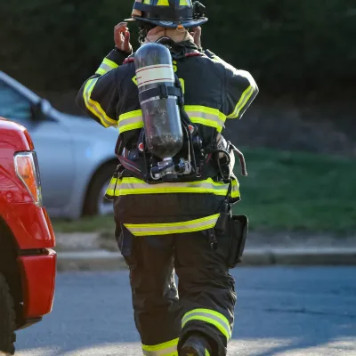 Firefighter adjusting helmet walking on street wearing full protective gear and oxygen tank on back.
