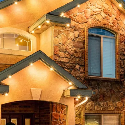 Stone and stucco house exterior with warm lighting under eaves at dusk