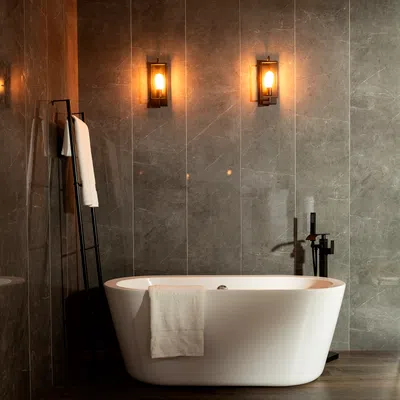 Modern bathroom with a white freestanding bathtub, towel rack, and two illuminated wall sconces on gray tiles.