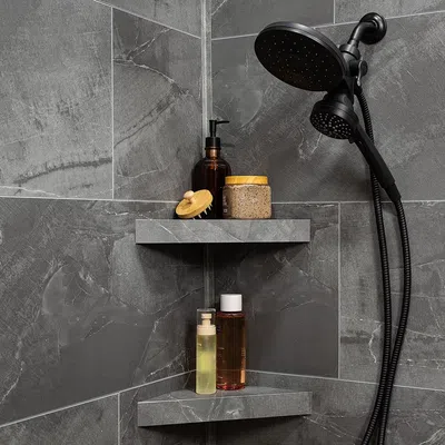 Black dual showerhead with gray tiled walls and shelves holding skincare products and a brush in a modern bathroom