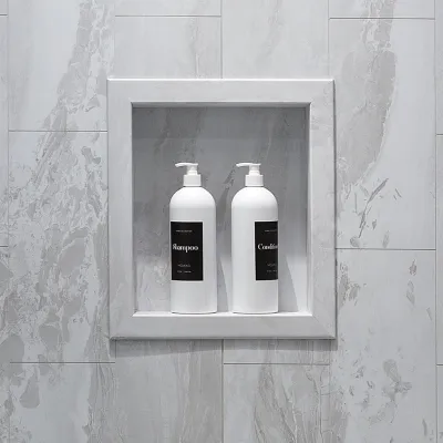 White shampoo and conditioner bottles with black labels in a marble shower niche with gray veining.