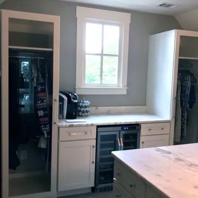 Walk in closet with a mini fridge for a champagne room, marble island, white cabinets, glass doors, hanging clothes and a window