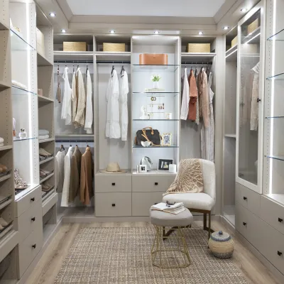 Custom walk-in closet with illuminated glass shelves, beige cabinetry, shoe shelving and clothing.