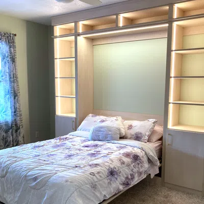 Cozy bedroom featuring a white bed with purple floral accents and wooden shelving, bathed in soft natural light.