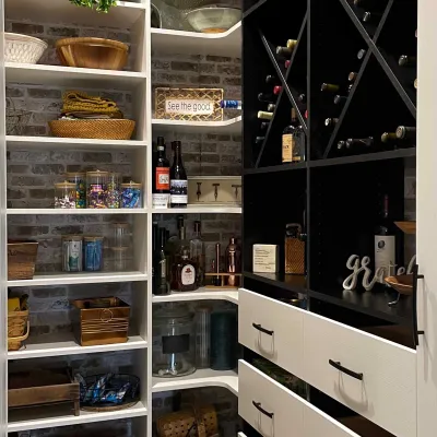 Organized pantry with shelves, baskets, wine racks, drawers, and decorative signs on a brick wall background