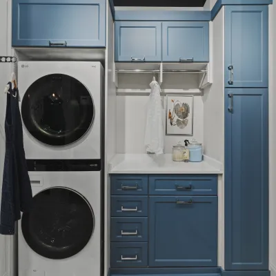 Modern laundry room with stacked white LG washer and dryer, blue cabinets, white countertop and hanging rod for clothing
