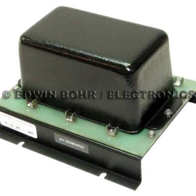 Black rectangular electronic transformer mounted on a green circuit board with metal clips and screws.