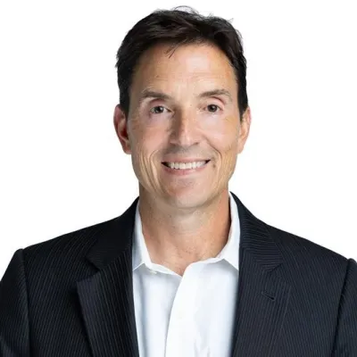 Professional middle-aged man in a black suit jacket and white shirt smiling against a white background