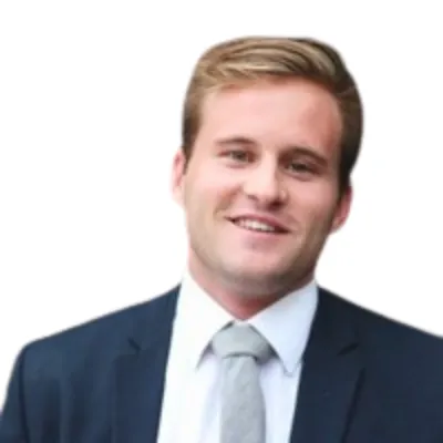 Smiling young man wearing a dark suit jacket, white shirt, and light gray tie against a white background