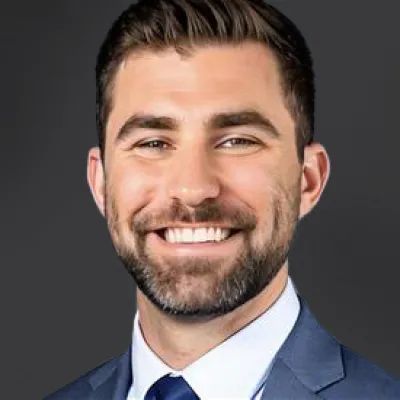 Smiling man in a suit against a dark background, representing professionalism and confidence.