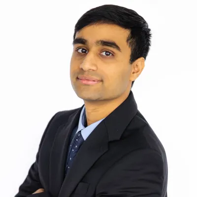 Professional young man in black suit with arms crossed confidently posing against white background