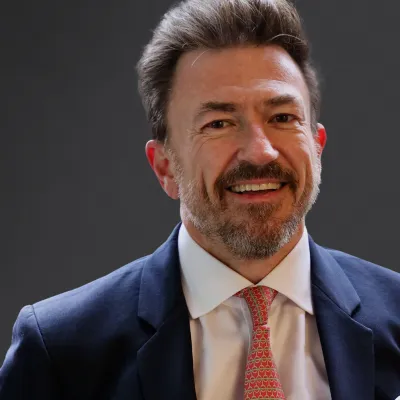 Smiling businessman in a suit, standing against a dark background, exuding professionalism and confidence.