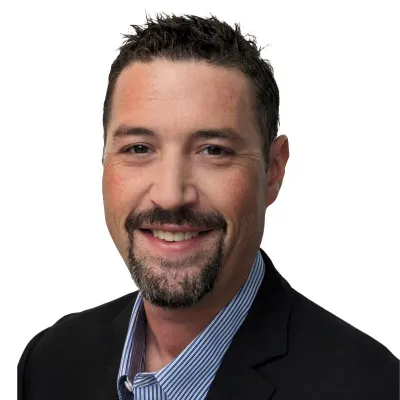 Drew Gamble smiling in black blazer and blue and white striped shirt