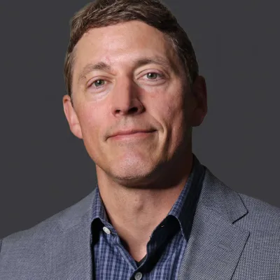 Portrait of a man in a gray blazer and checkered shirt against a dark gray background