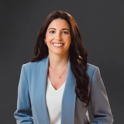Professional woman in a light blue blazer smiling confidently against a dark background.