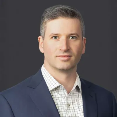 Professional man in a navy blazer and checkered shirt posing against a dark background