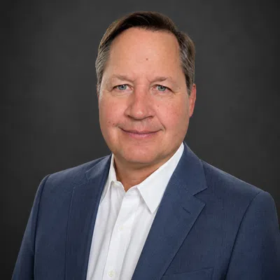 Professional middle-aged man wearing a blue suit jacket and white shirt against a dark background