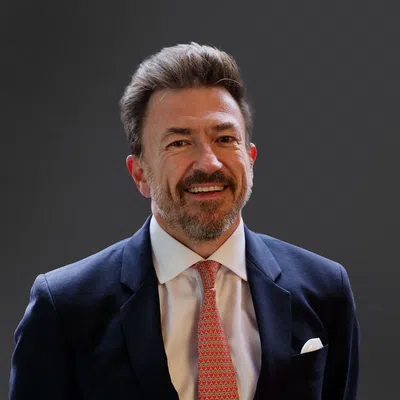 Smiling businessman in a suit, standing against a dark background, exuding professionalism and confidence.