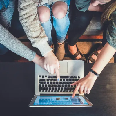 Three people pointing at a laptop screen while sitting on a patterned rug, collaborating closely.